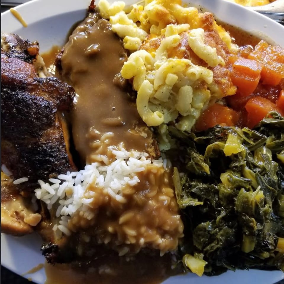 A soul food plate with baked chicken, rice and gravy, mac and cheese, candied yams, and collard greens.